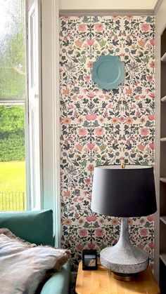 a living room with floral wallpaper and a blue lamp on a table in front of a window