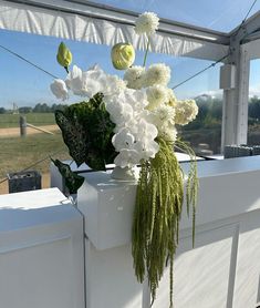 white flowers and greenery are in a vase on the window sill at an outdoor venue