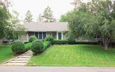 a house that is in the middle of some green grass and has trees around it