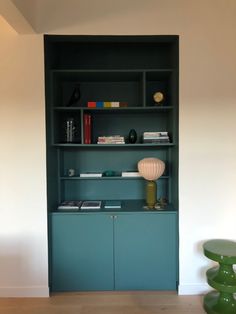 a green book shelf with books and other items on it in the corner of a room