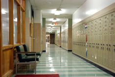 an empty hallway with lockers on the wall and chairs at the end in front of them