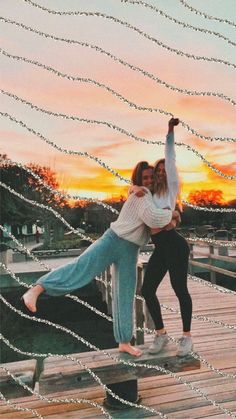 two women are standing on a dock with their arms in the air and one is holding her leg up