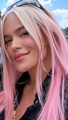 a woman with long pink hair and sunglasses on her head is smiling at the camera