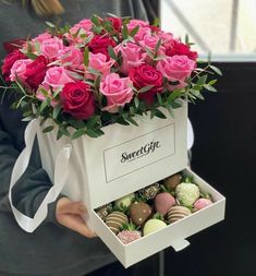 a woman holding a box full of pink roses and chocolate covered strawberries in it