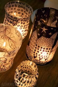 three lit candles sitting on top of a wooden table next to some glass containers with designs