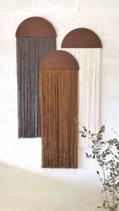 three wall hangings with different colors and fringes on the sides, one in brown, one in white