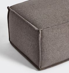 a grey square ottoman sitting on top of a white floor