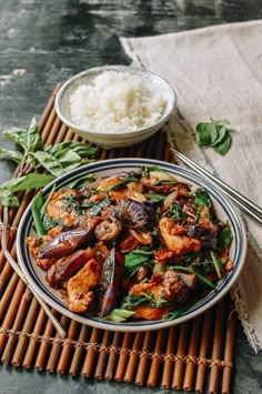 a plate full of food with rice and chopsticks next to it on a mat