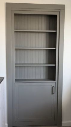 an empty bookcase in the corner of a room with white walls and gray flooring