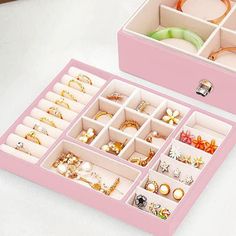 two pink boxes filled with different types of jewelry on top of a white table next to each other