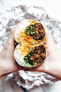 someone holding two burritos with meat and cheese