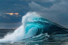 a large blue wave crashing into the ocean on a cloudy day with dark clouds in the background