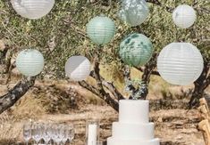 a table topped with a white cake and lots of paper lanterns hanging from the trees