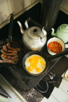 an image of eggs and bacon cooking on the stove top in the kitchen with tea kettle