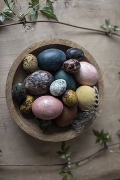 a wooden bowl filled with different colored eggs