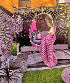 a pink blanket sitting on top of a wooden bench next to flowers and plants in front of a brick building