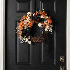 a black door with a wreath decorated with skulls, flowers and pumpkins on it