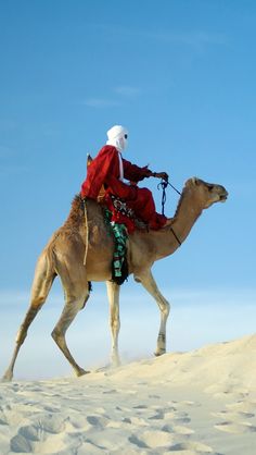 a man riding on the back of a camel in the middle of the sand dunes