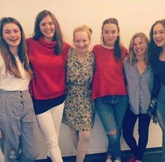 four girls are posing for the camera in front of a white wall and wearing red sweaters