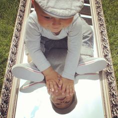 a young child is holding his hands in front of a mirror on the ground with grass