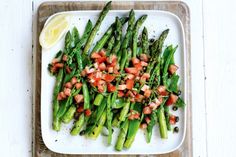 asparagus and tomato salad on a white plate with lemon wedges next to it