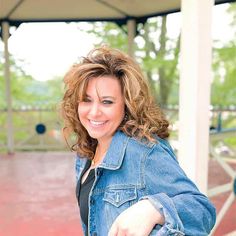 a woman in a denim jacket is smiling for the camera with her hand on her hip