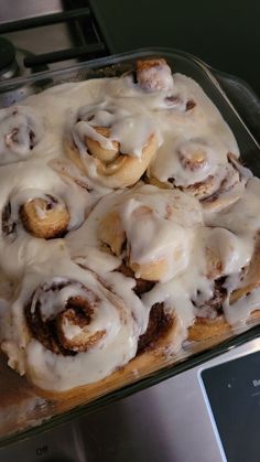 a glass baking dish filled with cinnamon rolls covered in icing on top of a counter