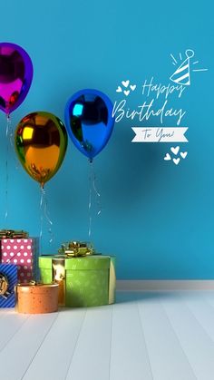 three balloons and presents are on the floor in front of a blue wall that says happy birthday to you