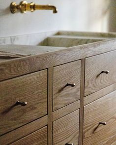 a wooden cabinet with brass handles and knobs in a bathroom sink, next to a faucet mounted on the wall