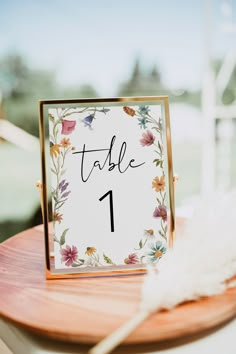 a table number is placed on top of a wooden board with flowers and feathers around it