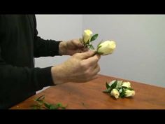 a man is arranging white roses on a wooden table in front of a wall,