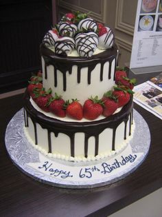 a three tiered cake with strawberries on top and chocolate drizzles