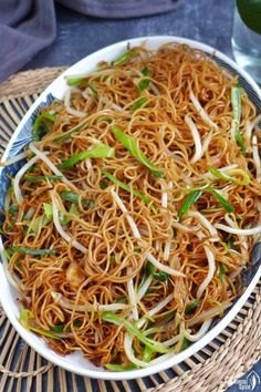 a white plate topped with noodles and veggies next to a glass of water