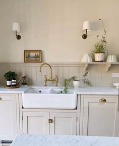 a kitchen with white cabinets and gold faucet, marble counter tops and brass fixtures