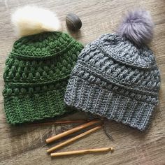 two crocheted hats sitting on top of a wooden table next to knitting needles