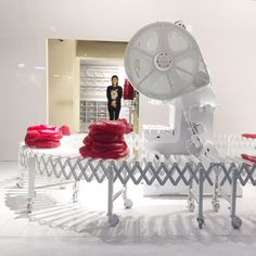 a woman standing next to a table with red objects on it and a fan in the middle