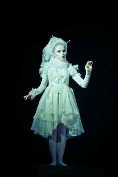 a woman in a white dress and headpiece standing on a black surface with her hands out