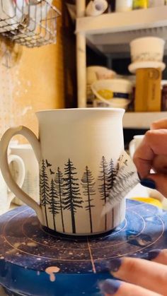 a person is painting a mug with trees on it