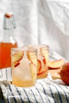 two jars filled with apple cider sitting on top of a table next to apples