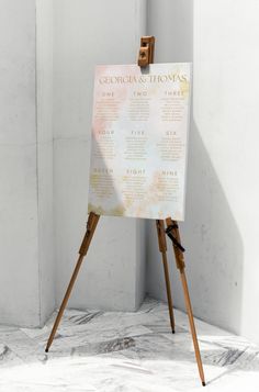 an easel stands in front of a white wall with a wedding seating chart on it