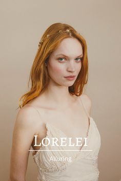 a woman with red hair wearing a white dress and gold headpiece, standing in front of a beige background