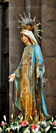 a statue of the virgin mary is shown in front of a floral arrangement on display