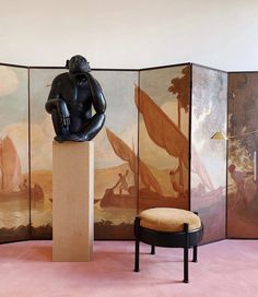 a room divider with paintings on the wall and a stool in front of it