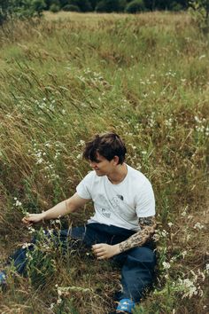 a young man sitting in the middle of a field with flowers on his leg and arm