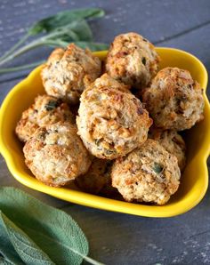 a yellow bowl filled with meatballs on top of a wooden table next to green leaves