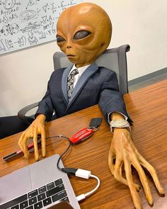 an alien head sitting on top of a desk next to a laptop