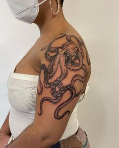 a woman wearing a face mask with an octopus tattoo on her left shoulder and chest