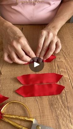 a woman is cutting out red ribbon on a wooden table with scissors and other crafting supplies