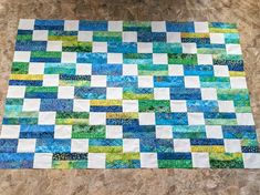 a blue and green patchwork quilt sitting on top of a tile floor next to a wall