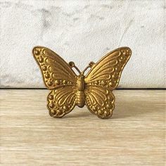 a small gold butterfly sitting on top of a wooden table next to a white wall